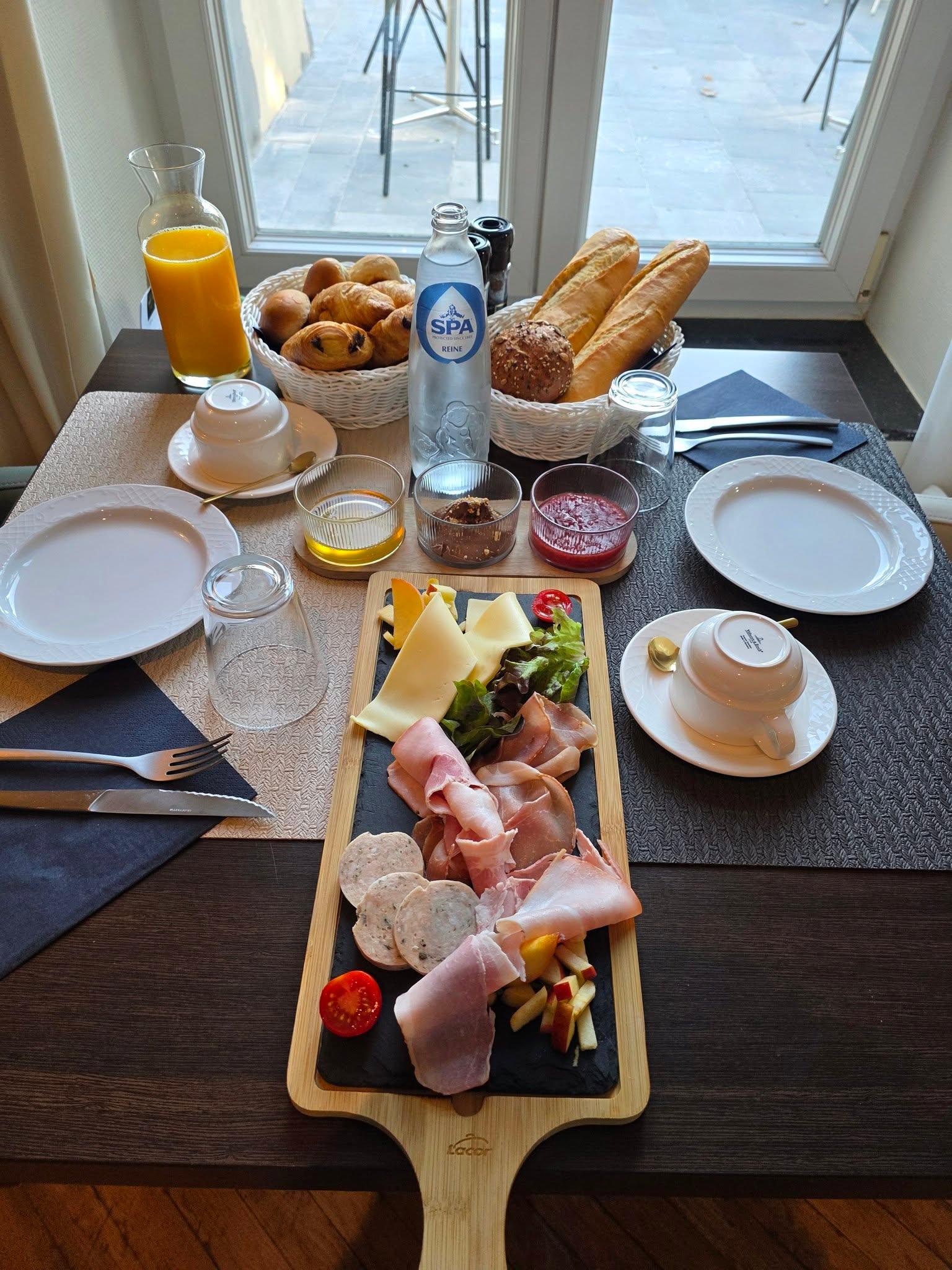 Gedeeld ontbijtplateau bij La Brasserie du Goût: gebak, brood, charcuterie, kazen, sinaasappelsap en koffie, gedekt bij het raam.