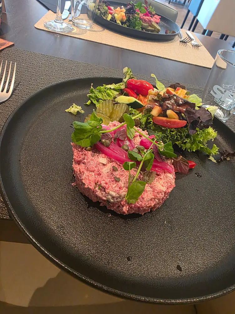 Américain dressé en cercle, oignons rouges marinés, cornichons, jeunes pousses et tomates