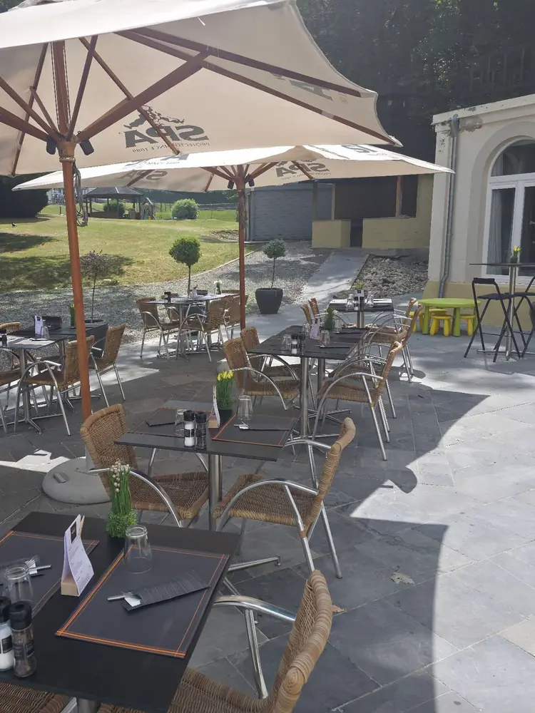 La terrasse de La Brasserie du Goût à Spa, tables et fauteuils en rotin sous de grands parasols, le jardin en arrière-plan